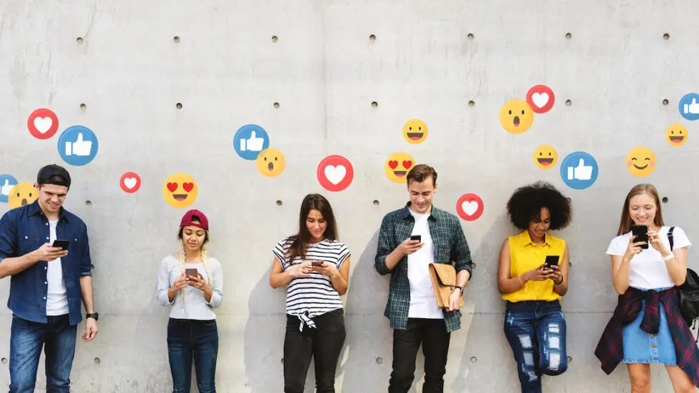 Image relating to "brands that work with micro influencer" story: six young adults interacting with their phones. Thumbs-up, heart, and smiling face emoji float around