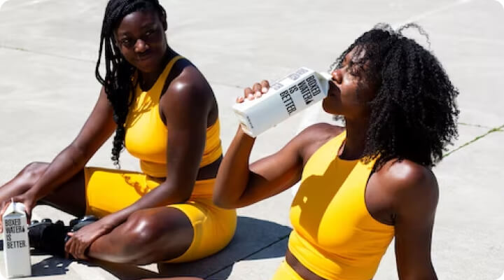 two female social influencers drinking boxes water in workout attire