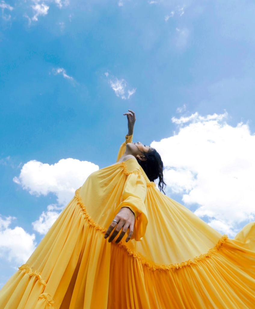 Female in yellow dress reaching for the sky