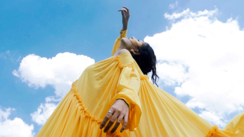 Female in yellow dress reaching for the sky