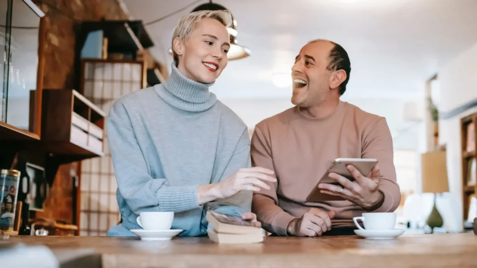 Influencer marketing for older generations: Two people sitting at a table in a coffee shop, looking at a tablet and react to what they see on the screen